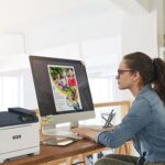 Una donna seduta alla scrivania, concentrata sul lavoro, con una stampante Xerox® C320 a colori