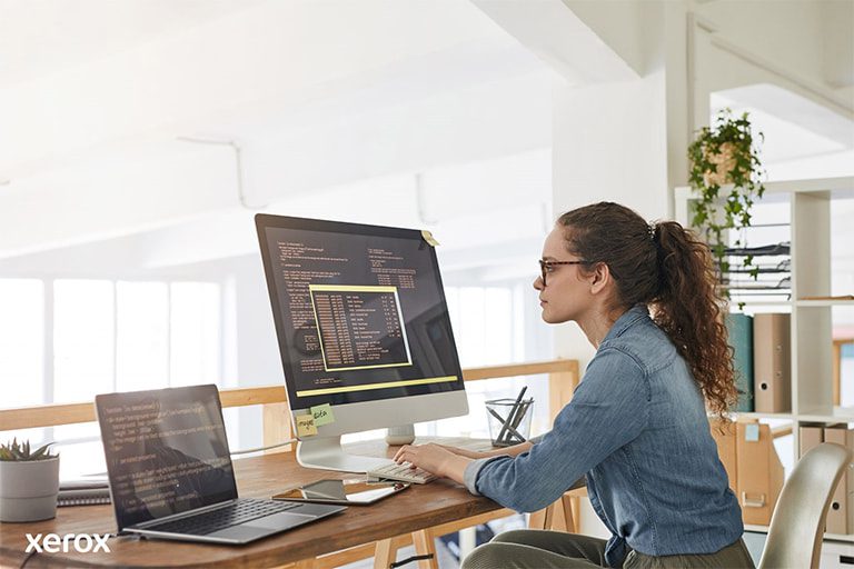 Una donna alla sua scrivania, impegnata con un computer e un laptop, dimostra produttività in uno spazio di lavoro moderno. Una donna alla sua scrivania, impegnata con un computer e un laptop, dimostra produttività in uno spazio di lavoro moderno.