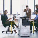 Xerox® VersaLink® C7100 Serie, stampante multifunzione a colori sul posto di lavoro Squadra al lavoro in un ufficio con carta stampata e la stampante multifunzione a colori Xerox® VersaLink® serie C7100